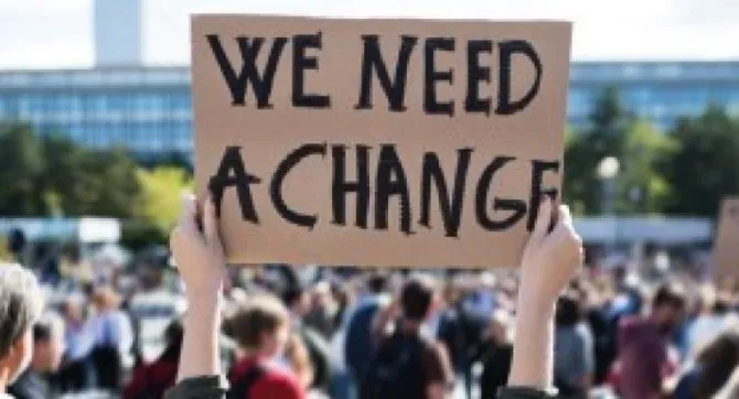 Bord met tekst 'We Need a Change' tijdens een demonstratie