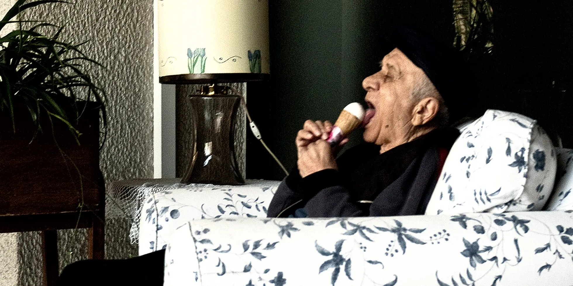 Bejaarde man in fauteuil eet ijsje.